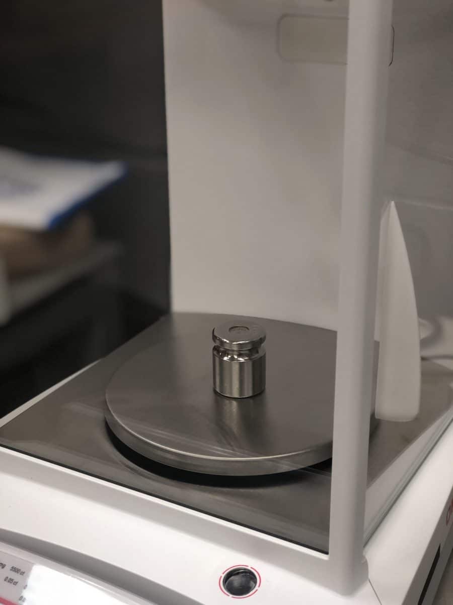 A test weight sits on the platter of a lab balance during calibration