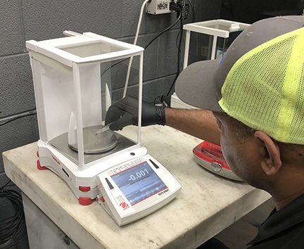 A calibration tech places a test weight on the platter of a lab balance