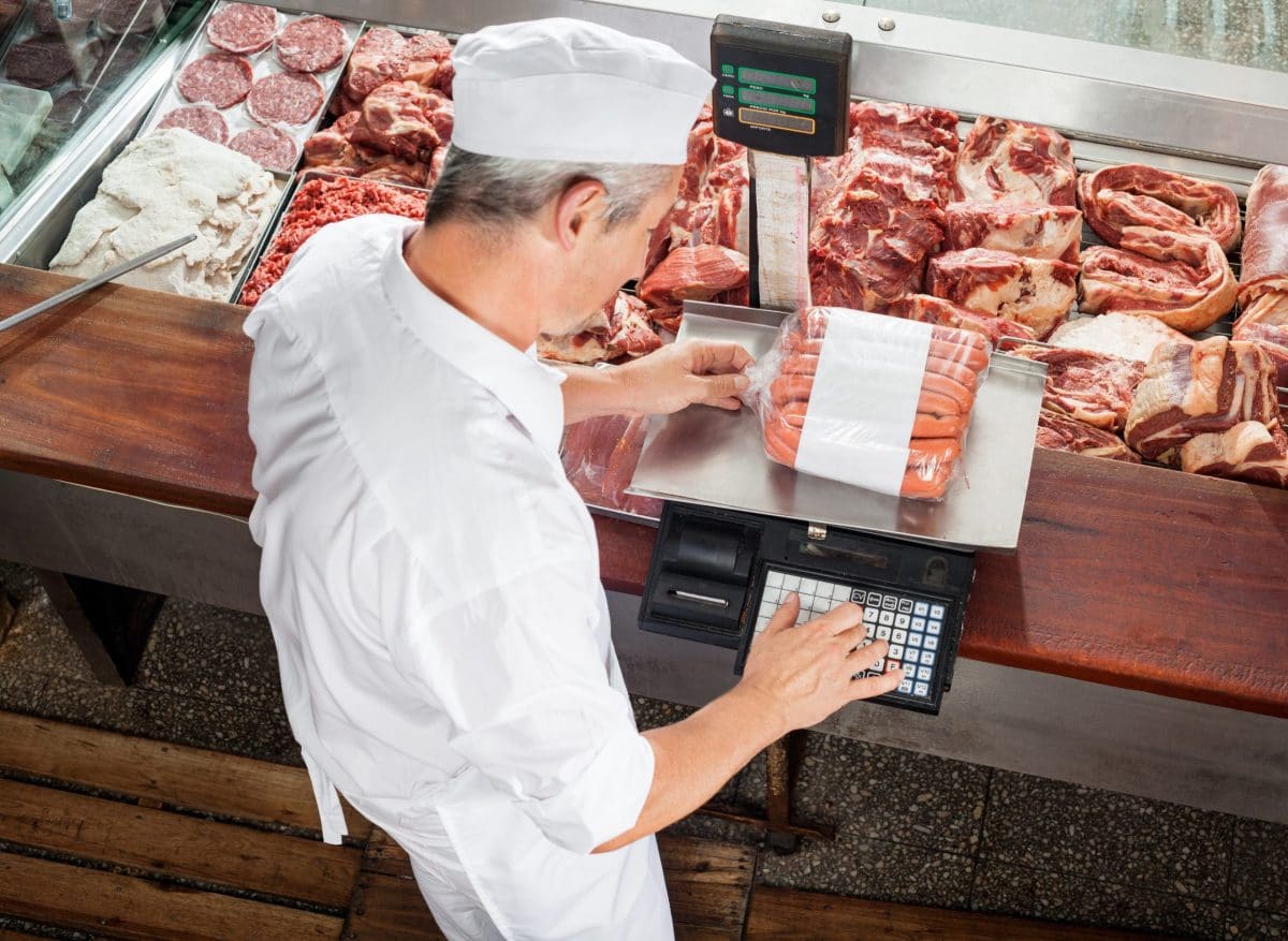 Butcher Weighing Sausages At Display Cabinet Butcher Weighing Sausages At Display Cabinet