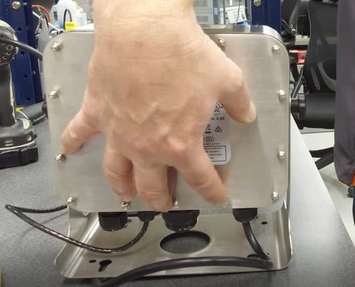 Technician hand can be seen as he performs equipment maintenance to check bolts on the back of a scale indicator