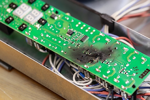 Close up burnt green microchip after short circuit due to water damage. Damaged overheat control panel board of cooking stove Microchip damaged by electric current