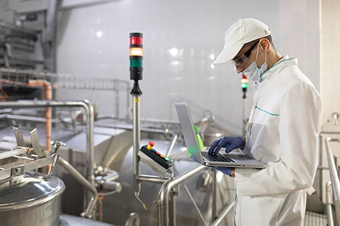 man in a white robe and a mask with a laptop in his hands is at the factory Technician with product inspection equipment