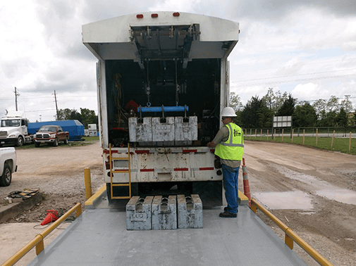 Truck Scale Calibration in Progress Michelli Weighing & Measurement service technician stands at the rear of a heavy duty test truck, using the remote to lower test weights onto a truck scale