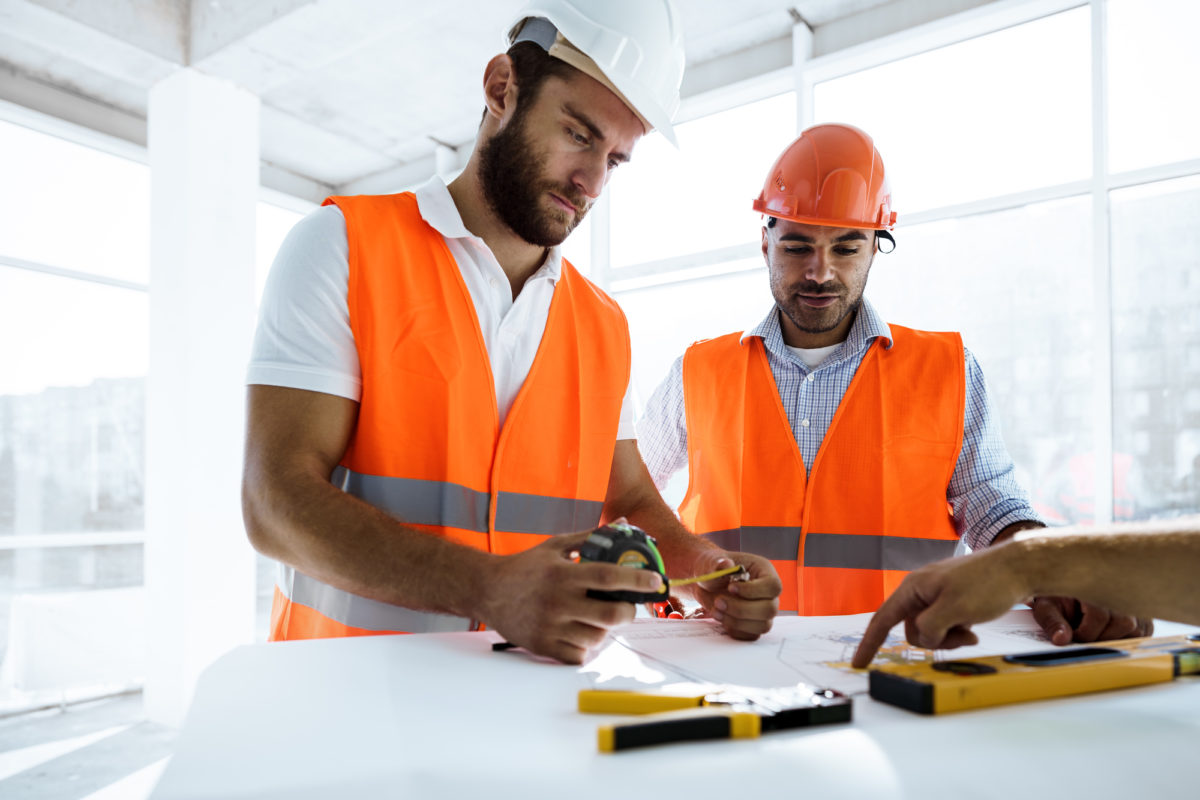 Two engineers collaborate and use accurate measurement equipment to look at plans on a table