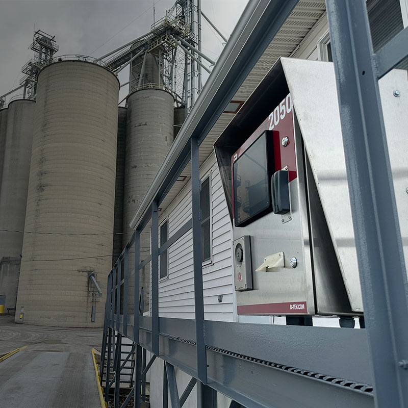 B-TEK Scales DD2050 indicator with truck scale visible and industrial silos in the background