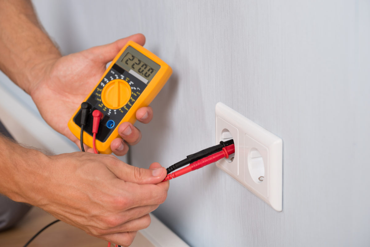 Person using a digital multimeter to measure electrical outlet voltage