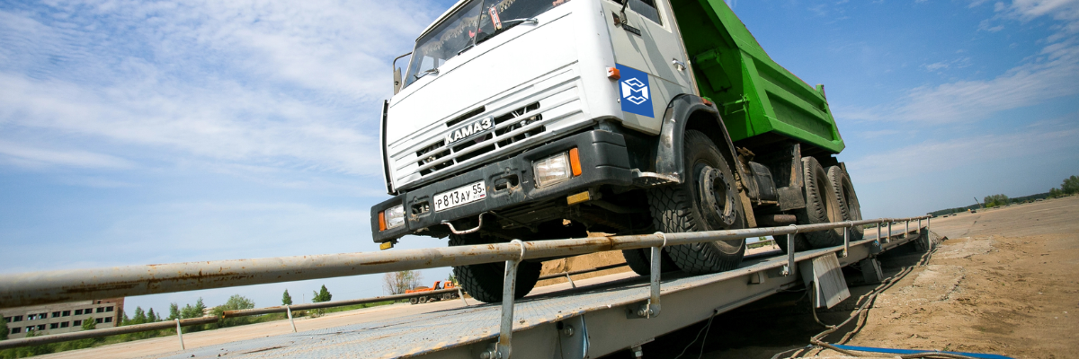 A large dump truck positioned on an industrial truck scale platform in an outdoor setting, demonstrating commercial vehicle weighing in progress.