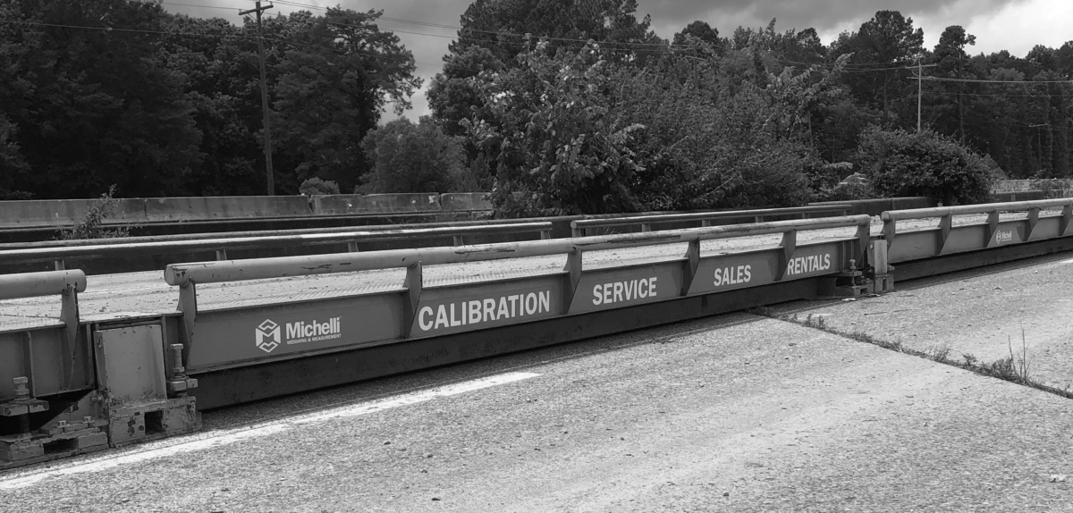 Michelli rental truck scale deck on site A Michelli rental truck scale with magnets featuring the Michelli Weighing & Mesaurement logo and the words Calibration, Service, Sales & Rentals on the side.