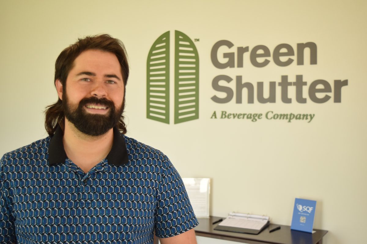 Lenny Zichichi, COO, Green Shutter Tea smiles in front of the Green Shutter Tea sign.