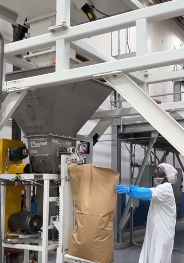 A worker packages tea into a brown paper bag using the quality control weighing system at Green Shutter Tea's facility